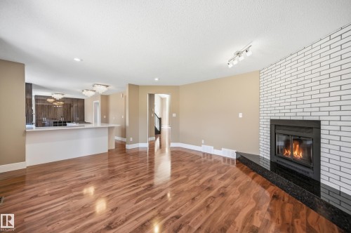 Living space featuring wood-finish flooring, a white brick fireplace with a black granite hearth, recessed lighting, and a track lighting fixture - 394 Walker Road, Edmonton, AB - Indoor Photo Showing Living Room With Fireplace