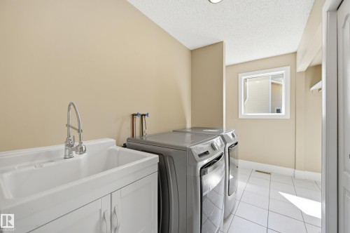 Dedicated laundry area featuring a utility sink with a chrome gooseneck faucet, white cabinet base, and a tiled floor - 394 Walker Road, Edmonton, AB - Indoor Photo Showing Laundry Room