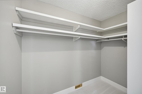 Spacious closet featuring dual-level shelving, integrated hanging rods, light gray wall paint, white baseboards, and a textured ceiling - 394 Walker Road, Edmonton, AB - Indoor With Storage