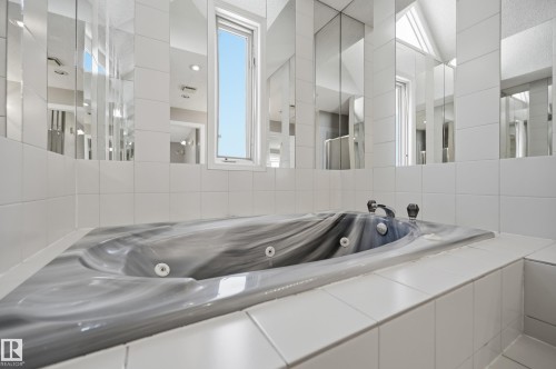 Jetted bathtub with a subtle marbled finish, surrounded by white square tile - 394 Walker Road, Edmonton, AB - Indoor Photo Showing Bathroom