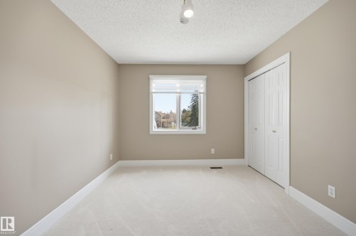 Carpeted room featuring a double-door closet, a window with a roller shade, light-colored walls, and a textured ceiling - 394 Walker Road, Edmonton, AB - Indoor Photo Showing Other Room