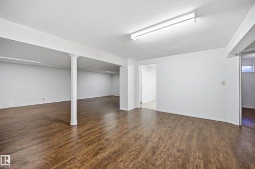 Spacious room featuring wood-finish flooring, white walls, and a textured white ceiling - 394 Walker Road, Edmonton, AB - Indoor Photo Showing Other Room