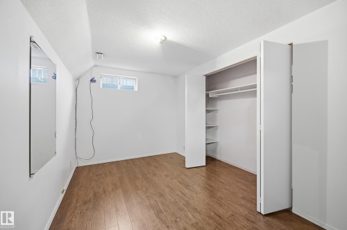 Room featuring wood-finish flooring, a built-in closet with bifold doors, integrated shelving, and a hanging rod - 394 Walker Road, Edmonton, AB - Indoor Photo Showing Other Room
