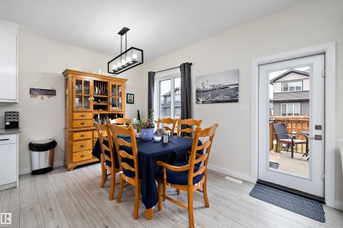 Dining area featuring light wood-finish flooring, a modern linear chandelier, and a glass-paneled exterior door - 82 Wingate Way, Fort Saskatchewan, AB - Indoor Photo Showing Dining Room