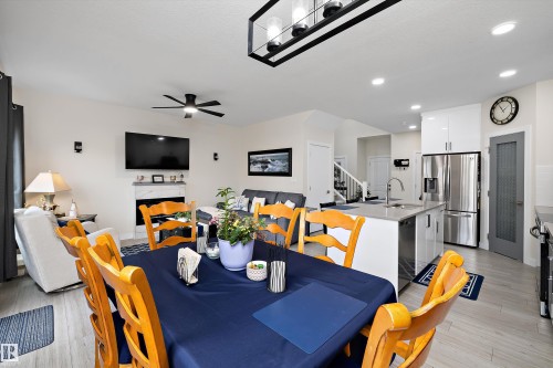 Open-concept living area featuring a modern kitchen island with a stainless steel sink, recessed lighting, wood-finish flooring, and a fireplace with a marble-style surround - 82 Wingate Way, Fort Saskatchewan, AB - Indoor Photo Showing Dining Room
