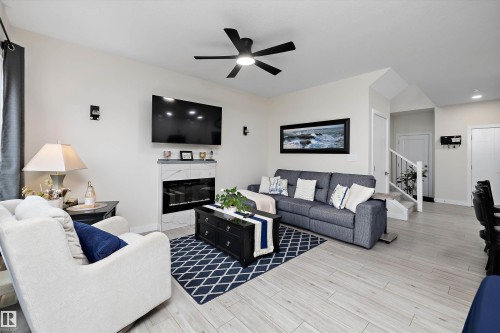 Living area featuring a modern fireplace with a light-colored surround, wood-finish flooring, a ceiling fan, and recessed lighting - 82 Wingate Way, Fort Saskatchewan, AB - Indoor Photo Showing Living Room