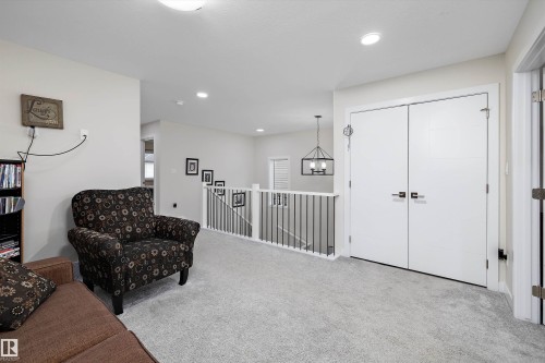 Second-story landing featuring soft grey carpeting, a white baluster railing with black metal spindles, and a contemporary black metal framed chandelier - 82 Wingate Way, Fort Saskatchewan, AB - Indoor