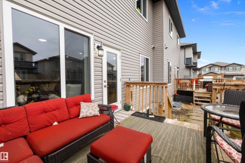 Rear exterior featuring a ground-level patio with a patterned outdoor rug, a sliding glass door, a separate exterior door with a wall-mounted light fixture, and horizontal siding - 82 Wingate Way, Fort Saskatchewan, AB - Outdoor With Deck Patio Veranda With Exterior