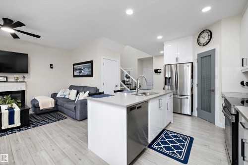 Open-concept living space featuring wood-finish flooring, a contemporary kitchen island with a built-in sink and dishwasher, white shaker-style cabinetry, and stainless steel appliances - 82 Wingate Way, Fort Saskatchewan, AB - Indoor Photo Showing Kitchen