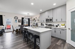 Open-concept kitchen and dining area featuring a central island with seating, grey cabinetry, stainless steel appliances, and wood-finish flooring - 