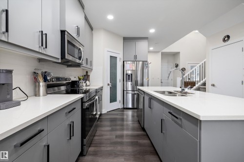 Contemporary kitchen featuring light gray cabinetry, stainless steel appliances, white countertops, and wood-finish flooring - 84 Wingate Way, Fort Saskatchewan, AB 