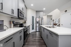 Contemporary kitchen featuring light gray cabinetry, stainless steel appliances, white countertops, and wood-finish flooring - 