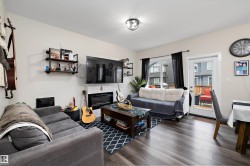 Open living area featuring wood-finish flooring, a contemporary fireplace, and a glass-paneled door leading to an exterior deck - 
