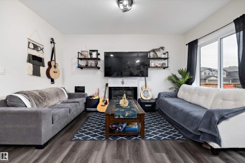 Spacious living area featuring wood-finish flooring, a built-in fireplace with a white mantle, and a ceiling-mounted light fixture - 84 Wingate Way, Fort Saskatchewan, AB 