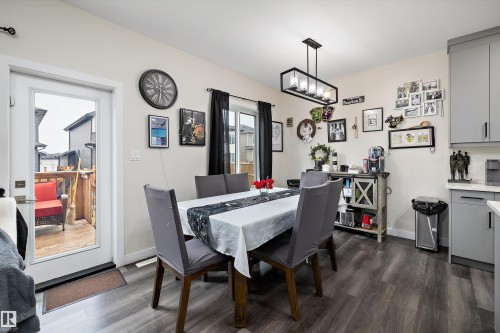 Dining area featuring wood-finish flooring, a contemporary linear chandelier, and a white framed patio door - 84 Wingate Way, Fort Saskatchewan, AB 