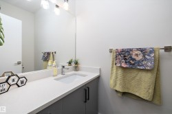 Spacious bathroom featuring a rectangular undermount sink, light-toned countertop, dark wood-finish cabinetry with black hardware, a large wall-mounted mirror, and a three-bulb vanity light fixture - 