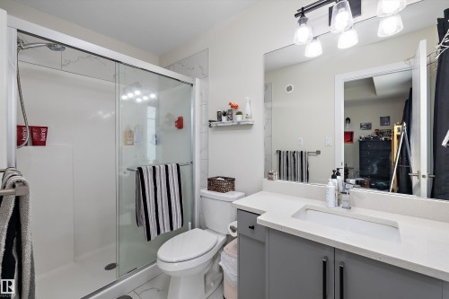 Contemporary bathroom featuring a glass-enclosed shower, a light-toned vanity with an integrated sink, a large wall-mounted mirror, modern overhead lighting, and a white toilet - 84 Wingate Way, Fort Saskatchewan, AB 