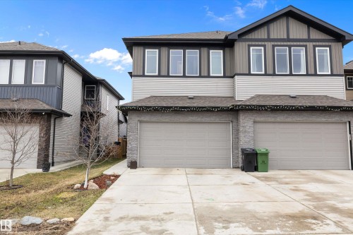 Modern duplex exterior featuring a two-car garage, stone veneer siding, light gray horizontal siding, dark vertical siding, and a concrete driveway - 84 Wingate Way, Fort Saskatchewan, AB 