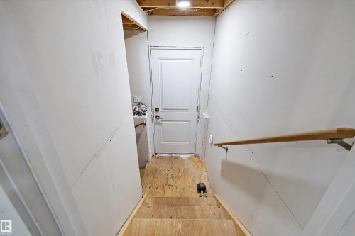 Unfinished basement stairs featuring plywood treads and risers, a wood handrail with metal brackets, and drywall walls - 84 Wingate Way, Fort Saskatchewan, AB 
