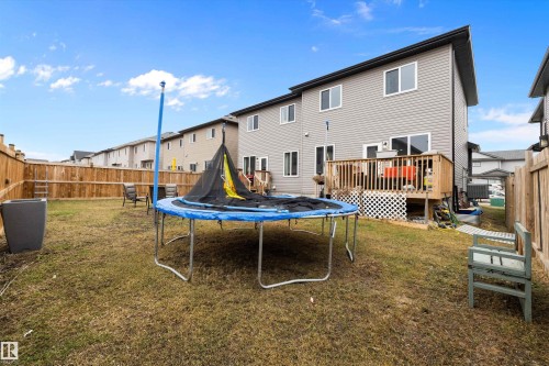 Spacious backyard featuring a wooden privacy fence, a multi-level deck with wooden railings, and gray vinyl siding on the property - 84 Wingate Way, Fort Saskatchewan, AB 