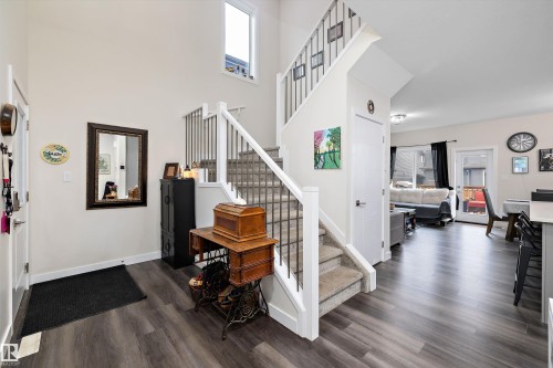 Foyer featuring an open-concept design with high ceilings, recessed lighting, wood-finish flooring, and a carpeted staircase with white risers and black metal spindles - 84 Wingate Way, Fort Saskatchewan, AB 