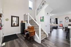 Foyer featuring an open-concept design with high ceilings, recessed lighting, wood-finish flooring, and a carpeted staircase with white risers and black metal spindles - 