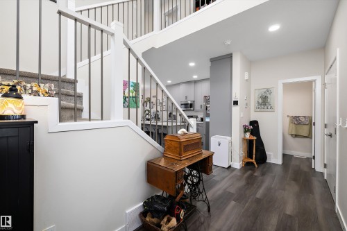 Open-concept entry with wood-finish flooring, a carpeted staircase with metal railings, and recessed ceiling lighting - 84 Wingate Way, Fort Saskatchewan, AB 