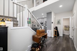 Open-concept entry with wood-finish flooring, a carpeted staircase with metal railings, and recessed ceiling lighting - 