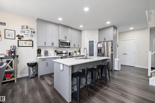 Modern kitchen featuring gray cabinetry, stainless steel appliances, an island with a white countertop, recessed lighting, and wood-finish flooring - 84 Wingate Way, Fort Saskatchewan, AB 