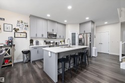 Modern kitchen featuring gray cabinetry, stainless steel appliances, an island with a white countertop, recessed lighting, and wood-finish flooring - 