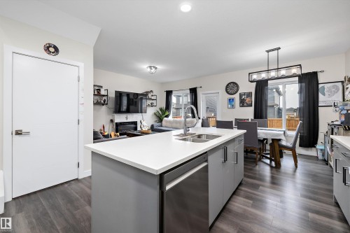 Open-concept kitchen featuring a central island with an integrated sink and stainless steel dishwasher - 84 Wingate Way, Fort Saskatchewan, AB 