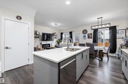 Open-concept kitchen featuring a central island with an integrated sink and stainless steel dishwasher - 