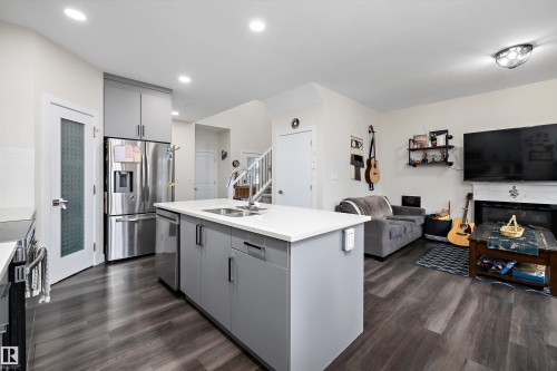 Open-concept interior featuring wood-finish flooring, a kitchen island with an integrated sink, stainless steel appliances, and a white countertop - 84 Wingate Way, Fort Saskatchewan, AB 