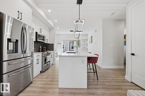 Modern kitchen featuring stainless steel appliances, white cabinetry with black hardware, an island with an integrated sink, and wood-finish flooring - 61 230 Edgemont Road, Edmonton, AB - Indoor Photo Showing Kitchen With Stainless Steel Kitchen With Upgraded Kitchen