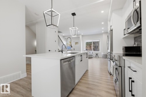 Modern kitchen island with a white countertop and integrated stainless steel dishwasher - 61 230 Edgemont Road, Edmonton, AB - Indoor Photo Showing Kitchen With Upgraded Kitchen