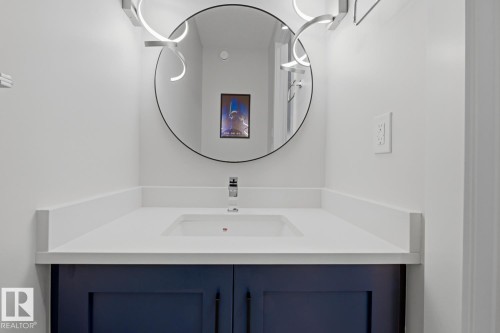 Vanity featuring a white countertop with an integrated rectangular sink, chrome faucet, and navy blue cabinetry - 61 230 Edgemont Road, Edmonton, AB - Indoor Photo Showing Bathroom
