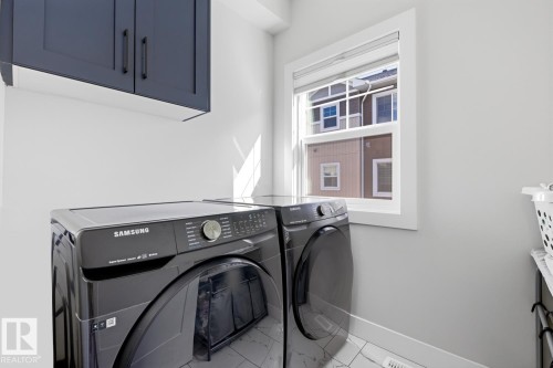 Laundry area featuring dark blue upper cabinetry with matte black hardware, light neutral wall paint, and a window with white trim - 61 230 Edgemont Road, Edmonton, AB - Indoor Photo Showing Laundry Room