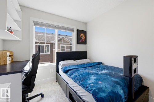 Bedroom featuring a large window, built-in shelving, a built-in desk with a dark countertop, and light-toned carpeting - 61 230 Edgemont Road, Edmonton, AB - Indoor Photo Showing Bedroom