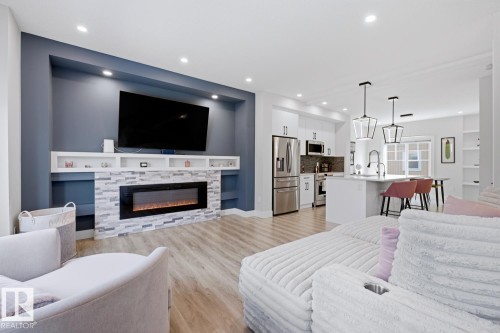 Open-concept living area featuring a stone-faced electric fireplace with built-in shelving, recessed lighting, and wood-finish flooring - 61 230 Edgemont Road, Edmonton, AB - Indoor Photo Showing Living Room With Fireplace
