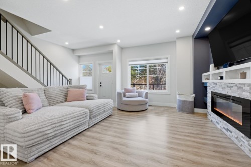 Living area featuring wood-finish flooring, recessed lighting, and a modern fireplace with stone surround and integrated shelving - 61 230 Edgemont Road, Edmonton, AB - Indoor Photo Showing Living Room With Fireplace