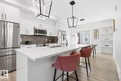 Open-concept kitchen featuring white cabinetry, stainless steel appliances, a tile backsplash, and a large island with a solid surface countertop - 61 230 Edgemont Road, Edmonton, AB - Indoor Photo Showing Kitchen With Stainless Steel Kitchen With Upgraded Kitchen
