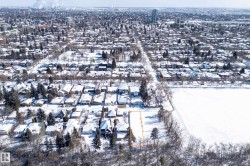 Aerial view showcasing the property within a snow-covered urban neighborhood, featuring residential homes with snow-dusted roofs and evergreen trees - 