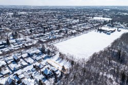 Aerial view of the property and surrounding neighborhood, featuring residential homes with snow-covered roofs and mature trees - 