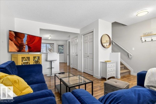Living area with wood-finish flooring, white walls, and a staircase featuring carpeted treads and a white handrail - 18 6032 38 Avenue, Edmonton, AB - Indoor Photo Showing Living Room