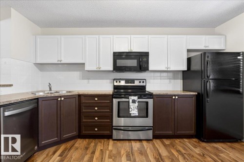 Kitchen with two-tone cabinetry, wood-finish flooring, a stainless steel range, and black refrigerator - 18 6032 38 Avenue, Edmonton, AB - Indoor Photo Showing Kitchen With Double Sink
