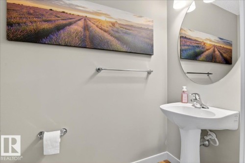 Pedestal sink with chrome faucet, complemented by an oval wall mirror and contemporary wall lighting - 18 6032 38 Avenue, Edmonton, AB - Indoor Photo Showing Bathroom