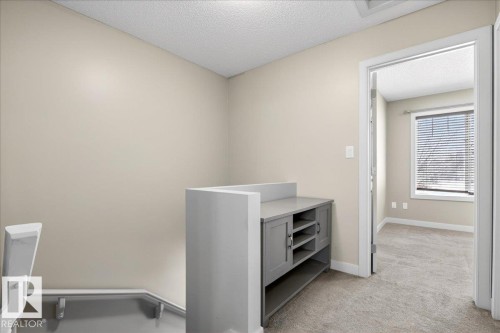 Upper-level landing featuring neutral-toned walls, textured carpet flooring, and a built-in grey console with open shelving - 18 6032 38 Avenue, Edmonton, AB - Indoor Photo Showing Other Room