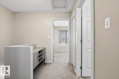 Hallway featuring light beige wall paint, light-colored carpet flooring, white trim, and a built-in grey cabinet with a countertop - 18 6032 38 Avenue, Edmonton, AB - Indoor