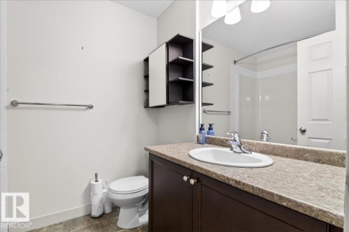 Bathroom featuring a dark wood-finish vanity with a light speckled countertop, an oval undermount sink, and a mirrored medicine cabinet with open shelving - 18 6032 38 Avenue, Edmonton, AB - Indoor Photo Showing Bathroom