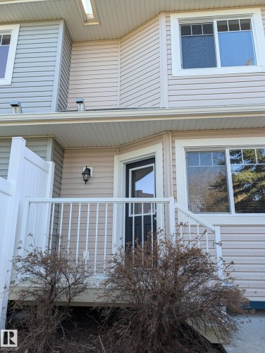 Property entrance featuring light beige horizontal siding, white trim windows, and a dark entry door with a storm door - 18 6032 38 Avenue, Edmonton, AB - Outdoor With Exterior